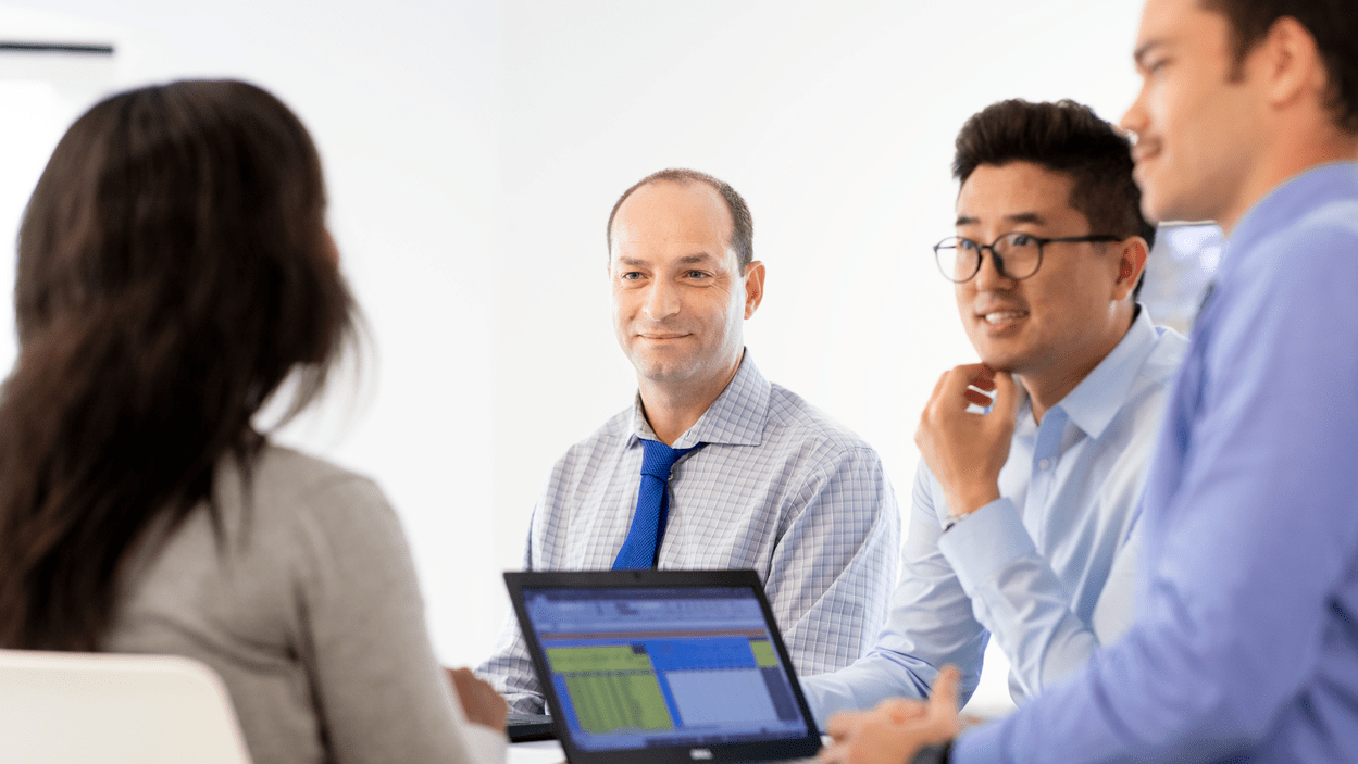 To menn og en dame ikledd skjorter smiler og ler i et møte.